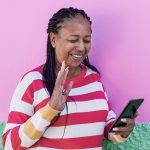 Side profile picture of woman against pink wall looking at the Floatpays app on her phone