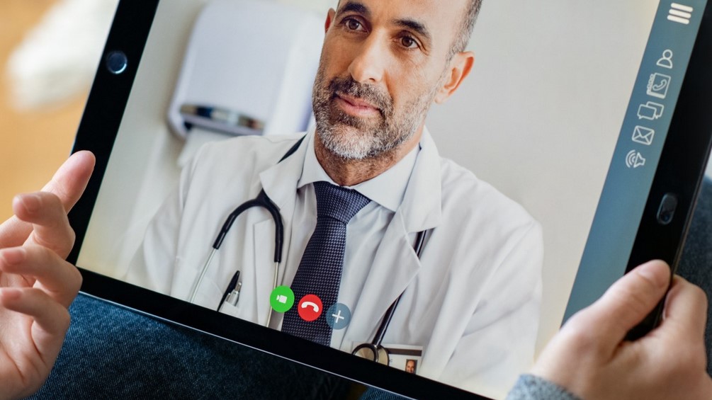 Image of a person's hands holding a tablet which has a medical video consultation with a DabaDoc doctor on it