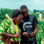 Image of farmers in a field looking ath ThriveAgric on a phone