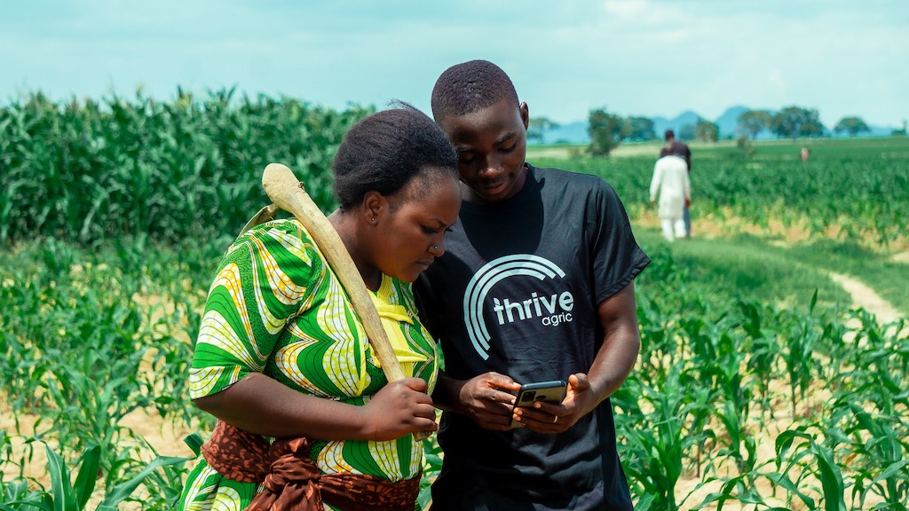 Image of farmers in a field looking ath ThriveAgric on a phone